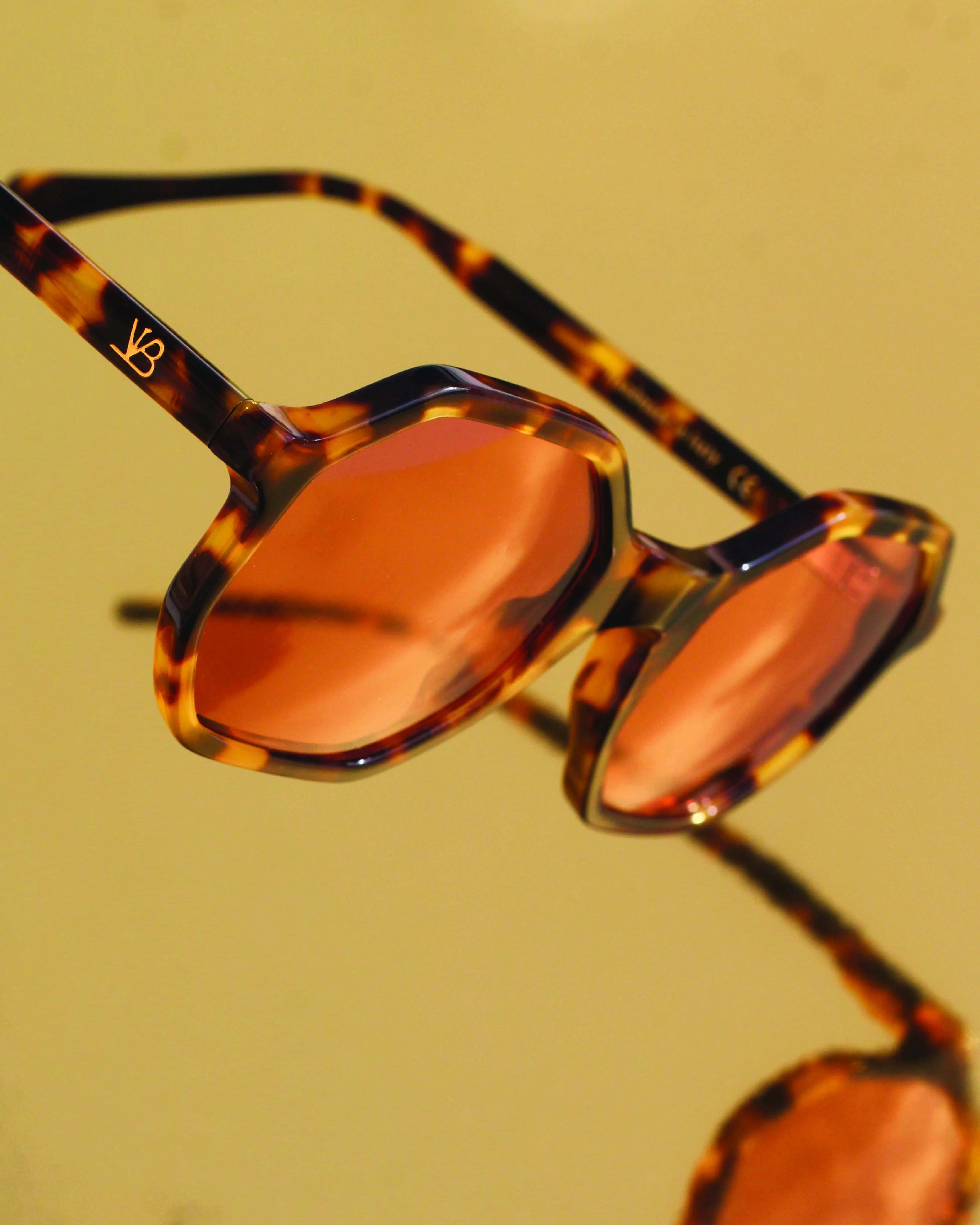 Sunglasses with tortoiseshell frame and orange lenses on a yellow background